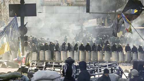 Varios manifestantes permanecen tras una barricada ante un cordón policial en Kiev (Ucrania) (Foto: EFE)