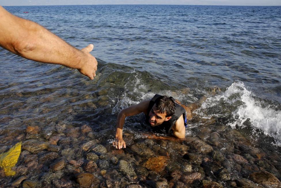 A local man helps a Syrian refugee who jumped off board from a dinghy as he swims exhausted at a beach on the Greek island of Lesbos September 17, 2015. REUTERS/Yannis Behrakis